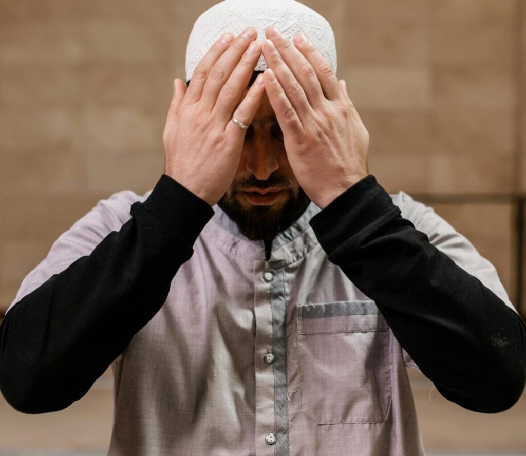 A man in traditional attire praying inside a mosque, symbolizing devotion.