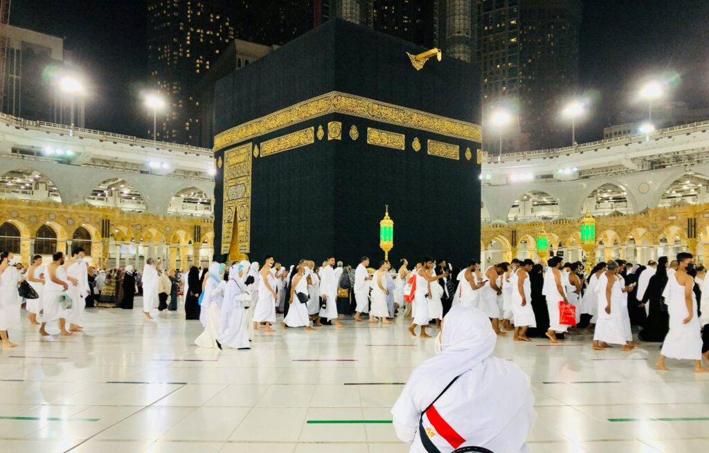 Muslim pilgrims perform Tawaf around the Kaaba in Mecca under bright lights at night.