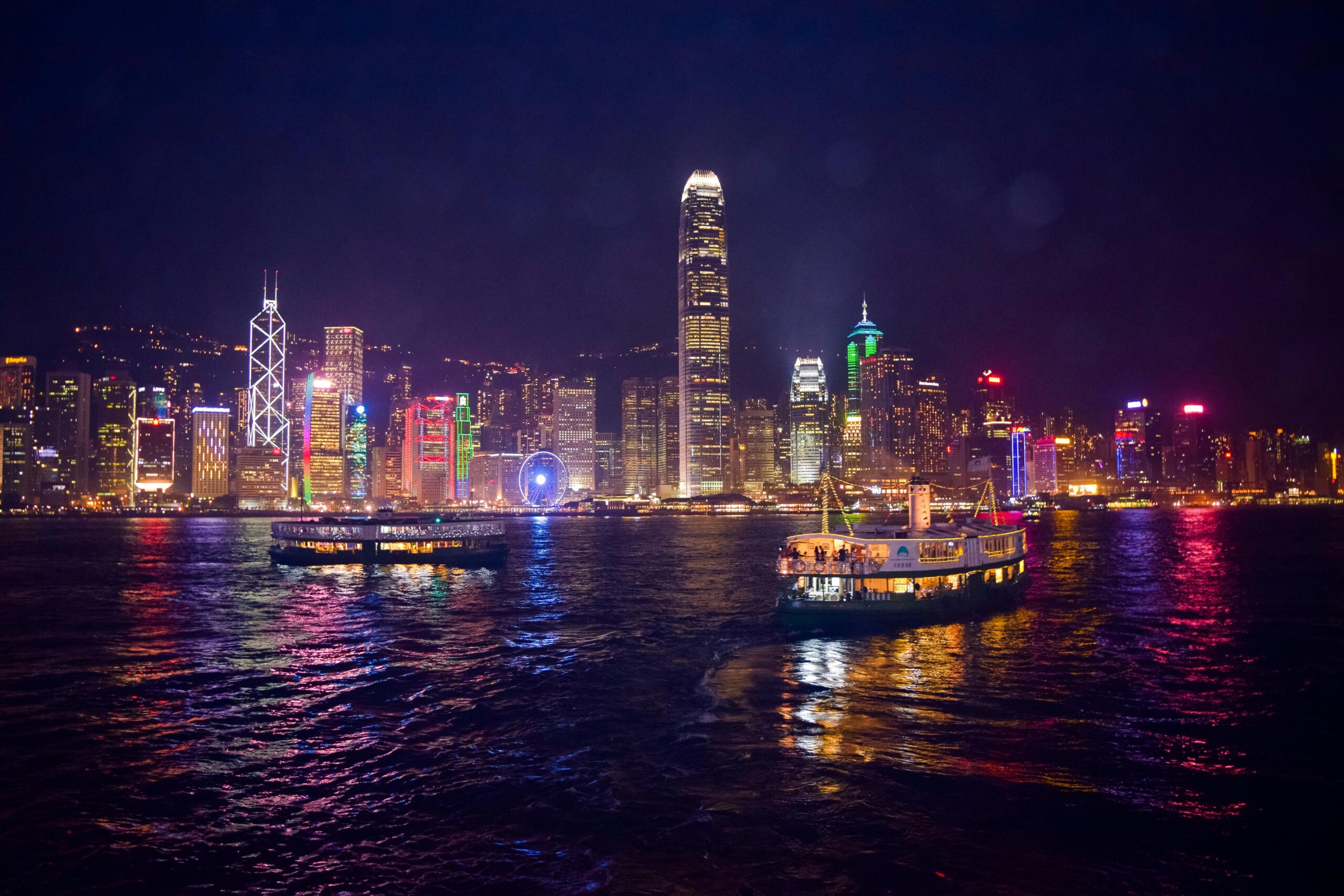 Captivating night view of Hong Kong's illuminated skyline and ferries reflecting on the water.