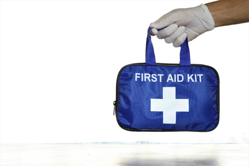 Close-up of a blue first aid kit held by a hand in a latex glove against an isolated white background.